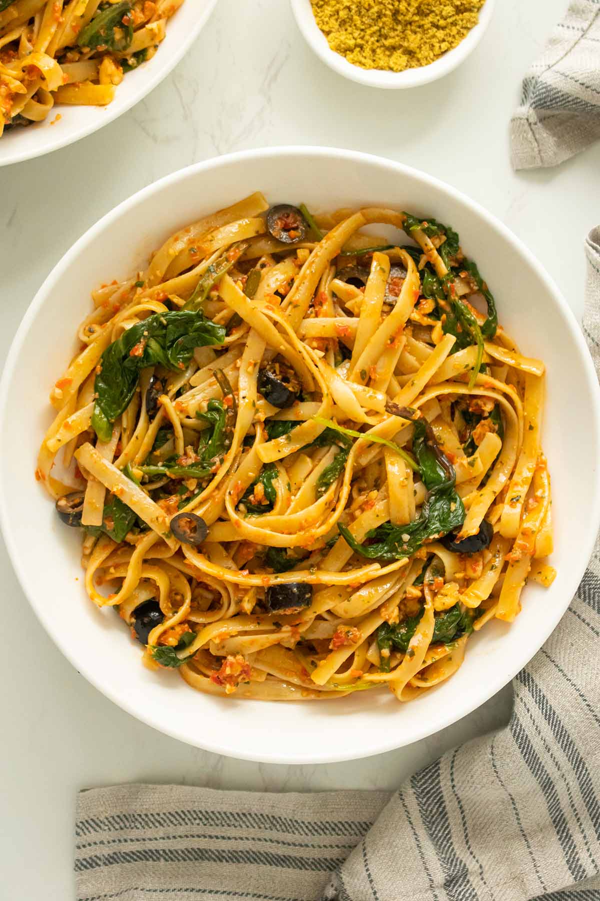 bowl of red pepper pesto pasta with spinach and black olives
