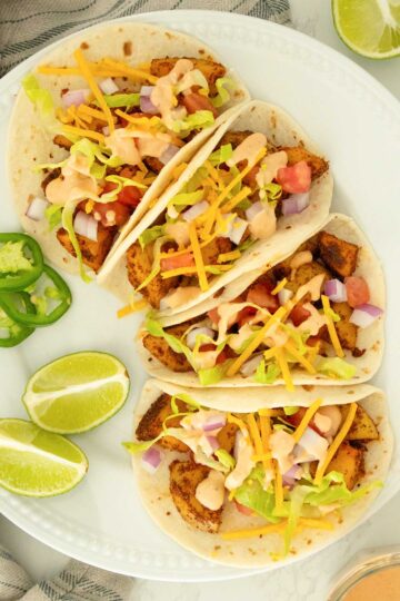 plate of spicy potato tacos topped with limes and jalapeño slices on the side