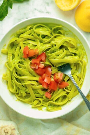 bowl of vegan avocado pasta topped with chopped tomato