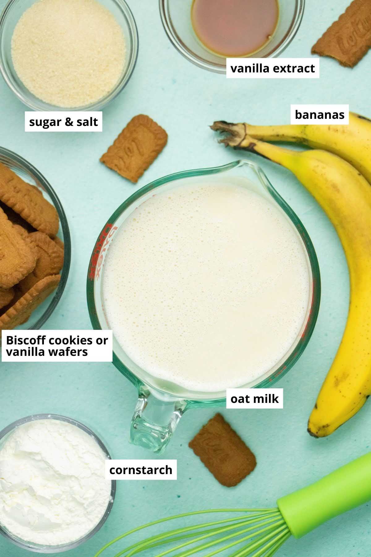 oat milk, cornstarch, vanilla, sugar, cookies, and bananas arranged on a blue table with a whisk