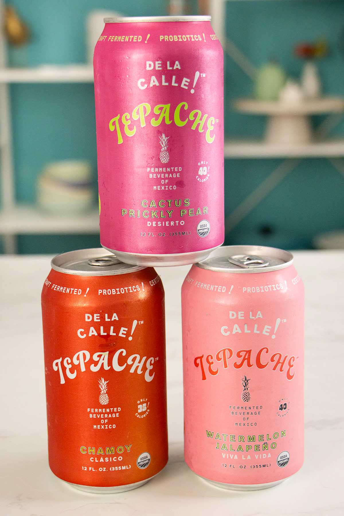 3 cans of De La Calle! Tepache on a white table: cactus prickly pear, chamoy, and watermelon jalapeño