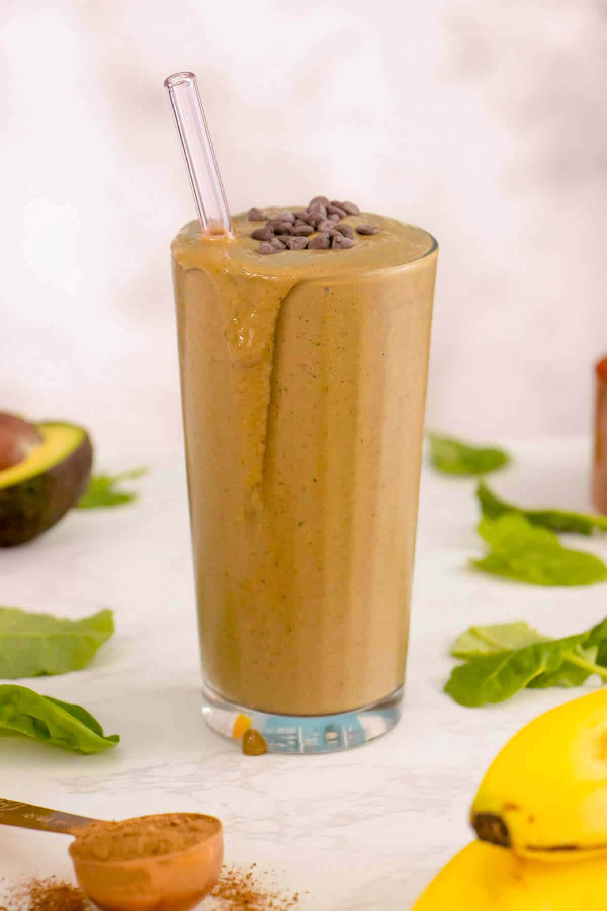chocolate spinach smoothie on a white table surrounded by some of the ingredients