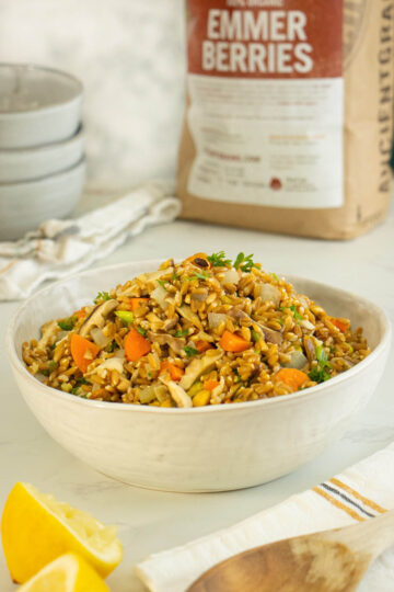 bowl of Instant Pot farro pilaf on a white table with a bag of emmer berries in the background