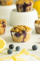 vegan lemon blueberry muffins on a white table with lemon slices and fresh blueberries