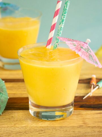 mango pineapple smoothies with umbrellas and straws in them on a wooden countertop