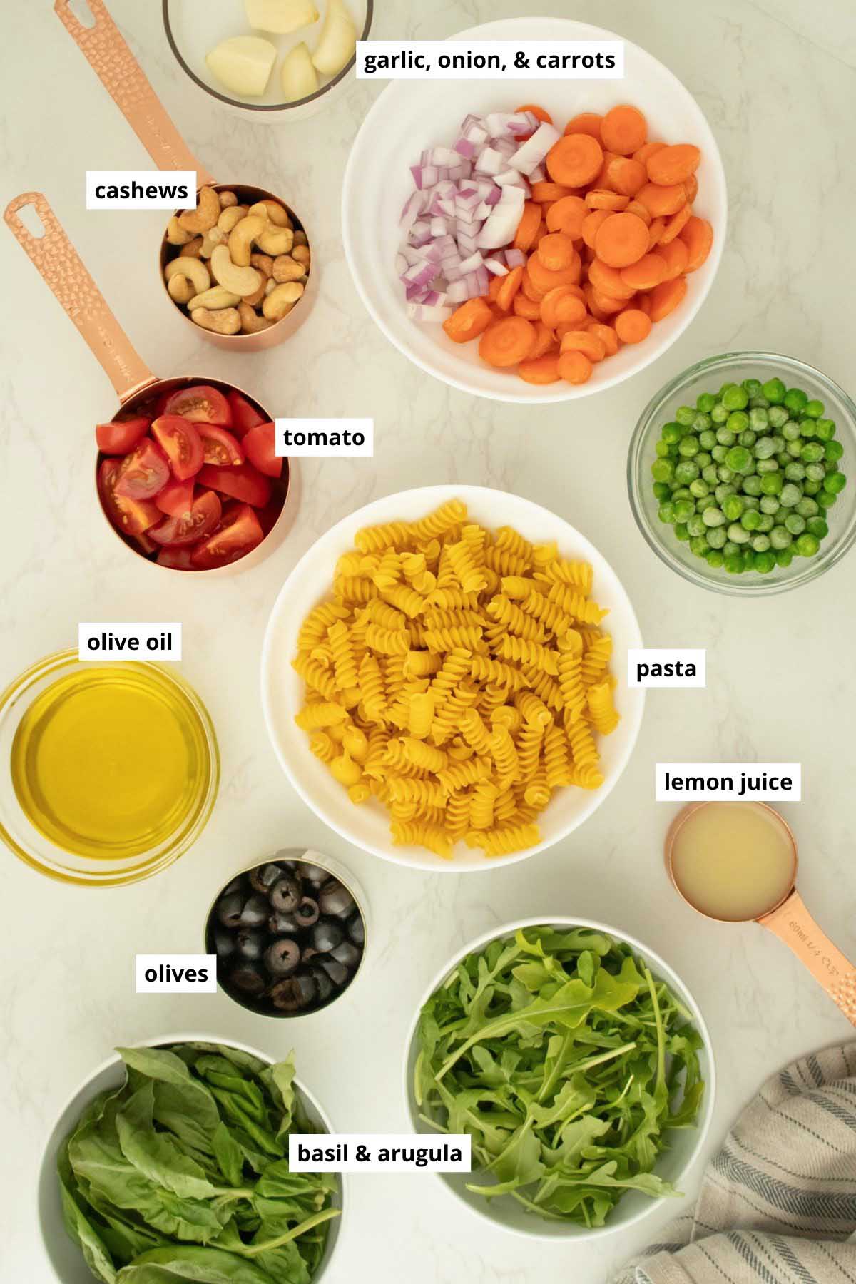 rotini pasta, basil, veggies, oil, lemon juice, and garlic with text labels on each ingredient