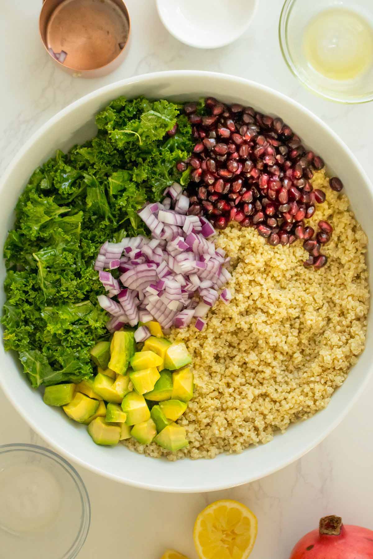 kale, quinoa, pomegranate seeds, red onion, and avocado in a mixing bowl before mixing