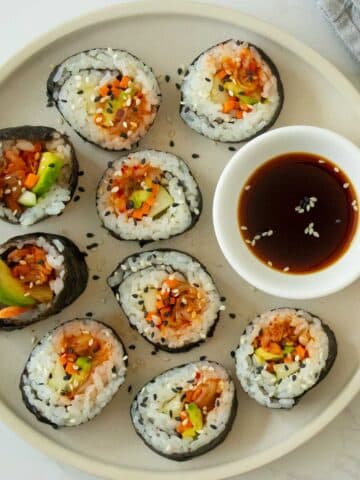 plate of kimchi sushi with sesame seeds and a side of soy sauce