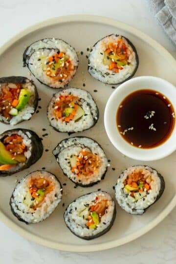 plate of kimchi sushi with sesame seeds and a side of soy sauce