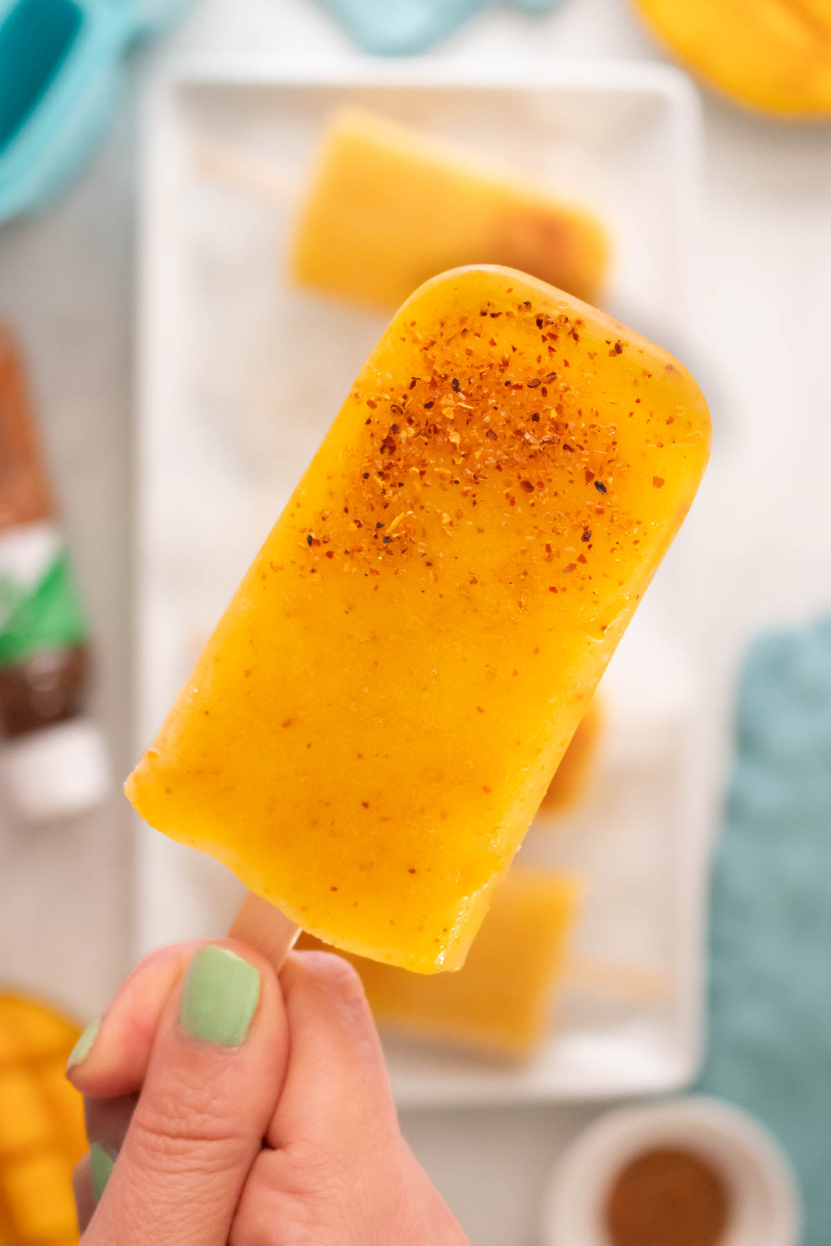 close-up of a hand holding a mango popsicle with Tajin