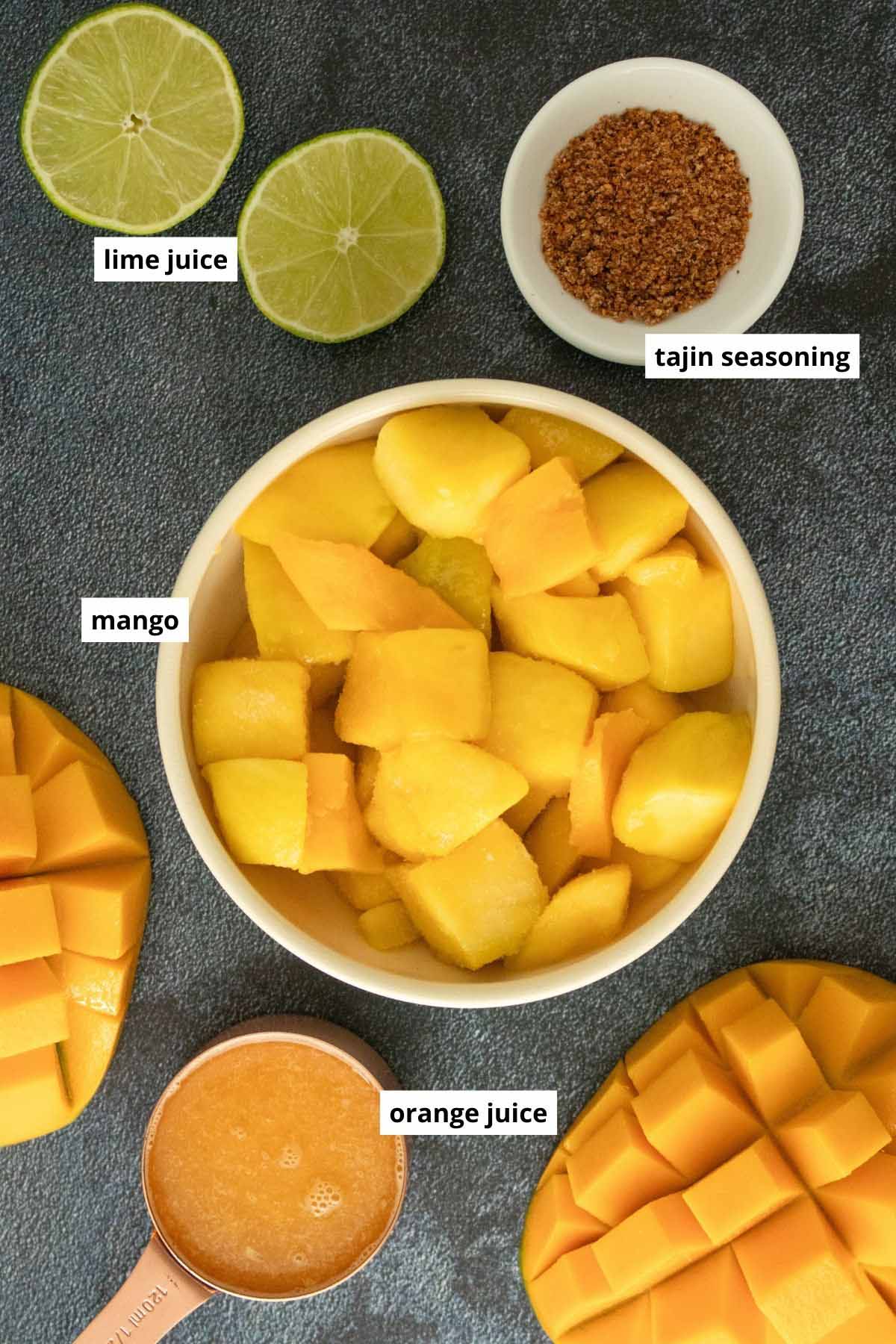 mango, tajin, orange juice, and lime halves on a dark tabletop