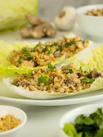 napa cabbage wraps on a white plate surrounded by toppings in bowls