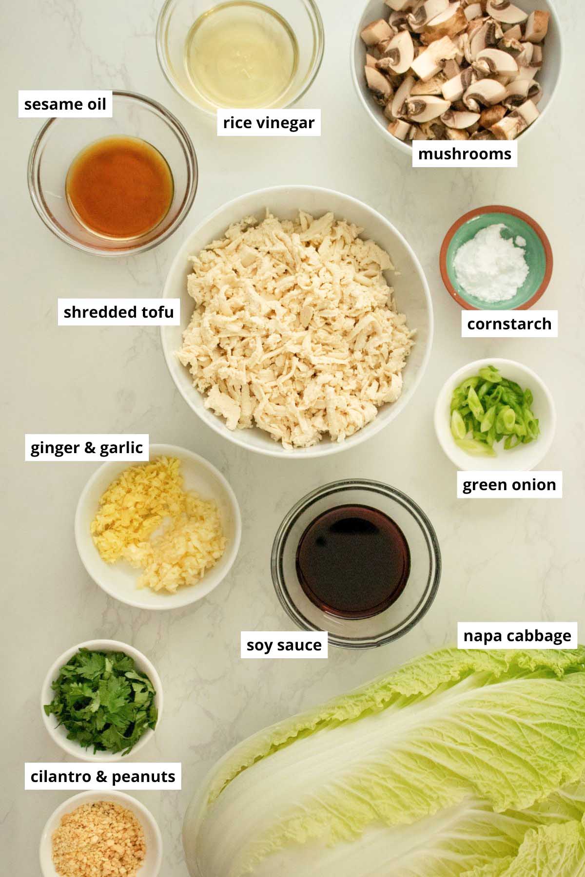 shredded tofu, Napa cabbage, and other wraps ingredients in bowls on a white table