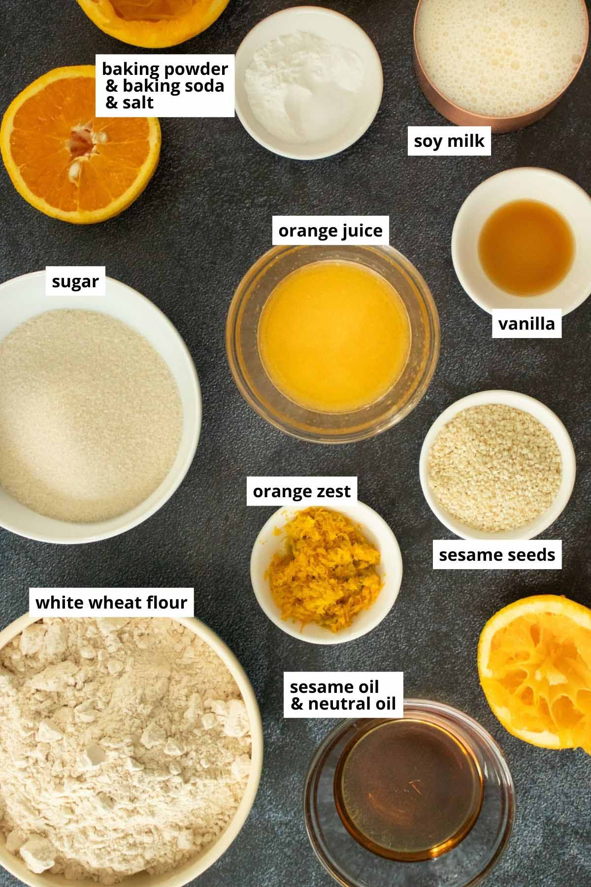 orange juice and zest, flour, sugar, and other muffin ingredients in bowls on a dark tabletop