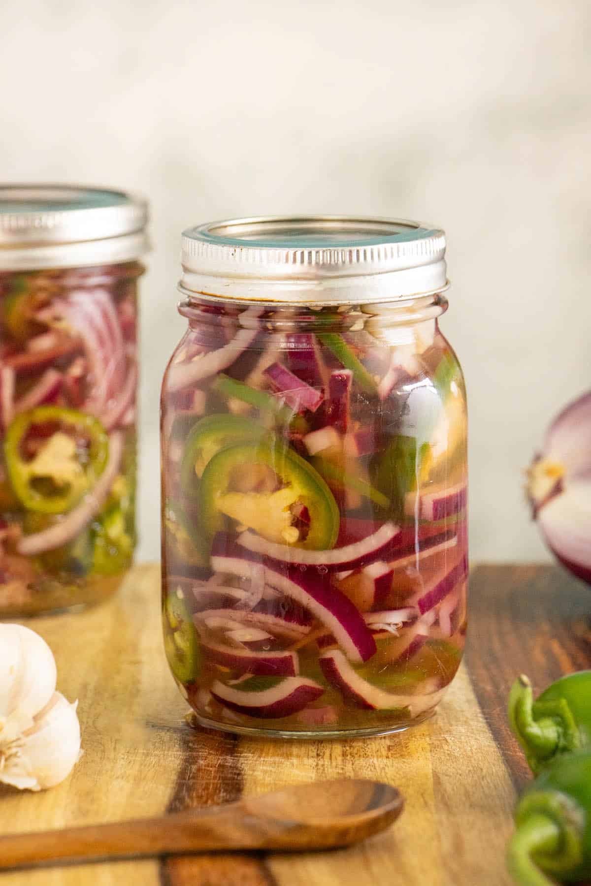 jars of pickled onions and on a wooden countertop with veggies around them