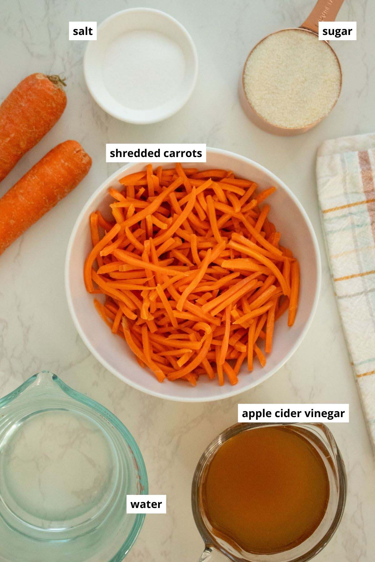 shredded carrots, sugar, salt, and vinegar in bowls and cups on a white table
