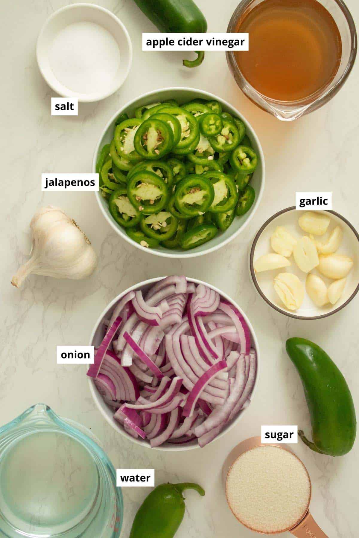 red onions, jalapeños, and other pickle ingredients in bowls on a kitchen counter