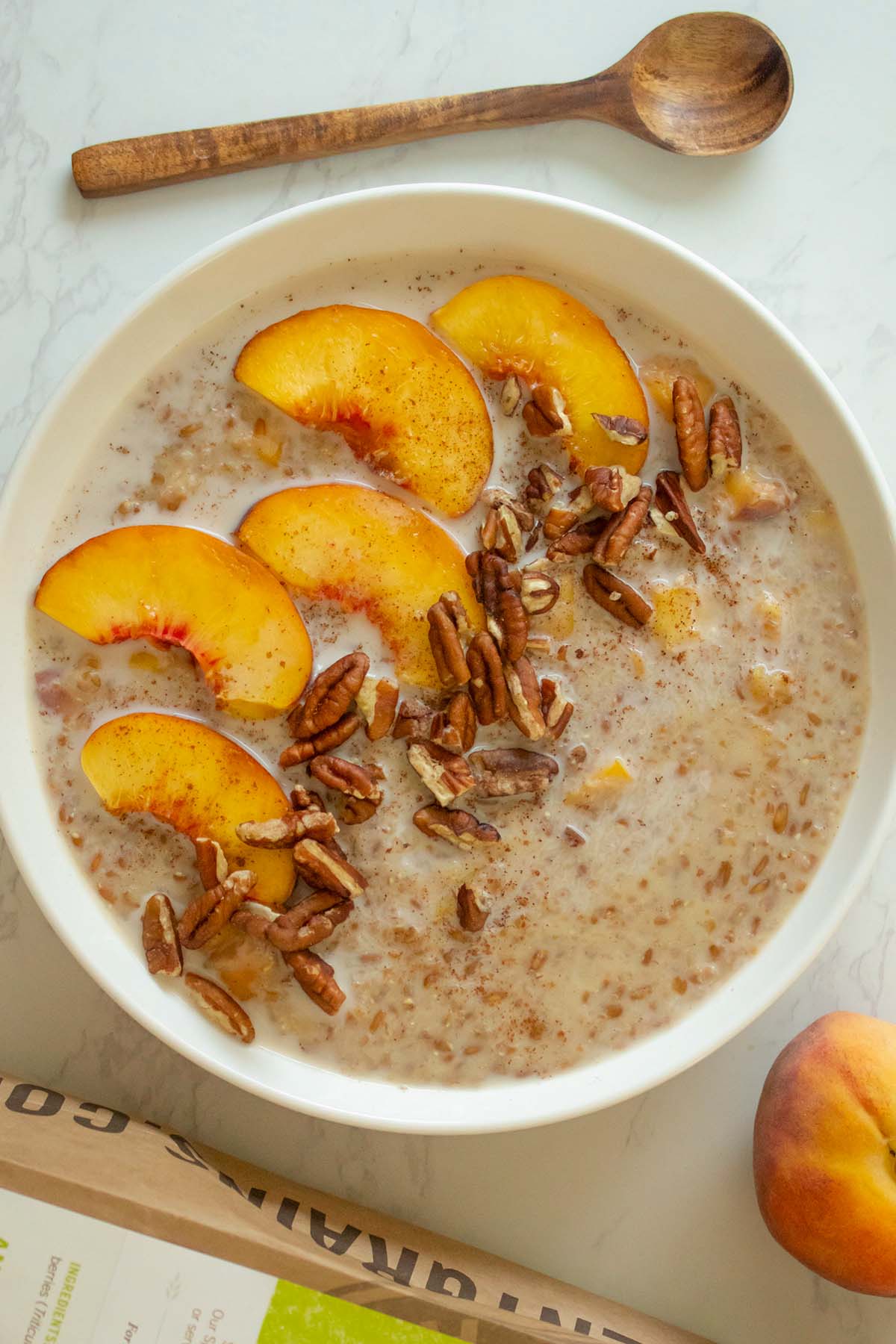 bowl of spelt porridge with peaches and pecans on a white table next to the storage bag