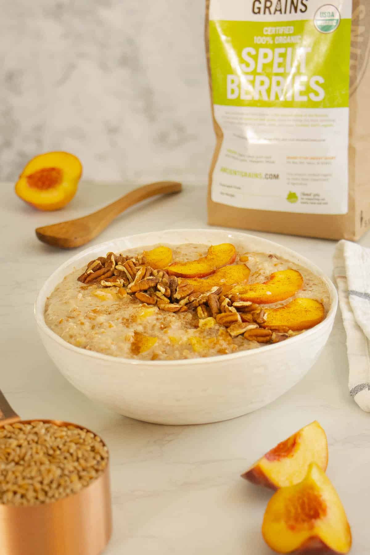 bowl of spelt porridge with peaches and pecans on a white table
