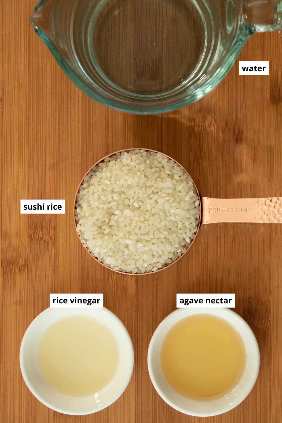 water, uncooked sushi rice, rice vinegar, and agave nectar arranged in cups on a wooden cutting board