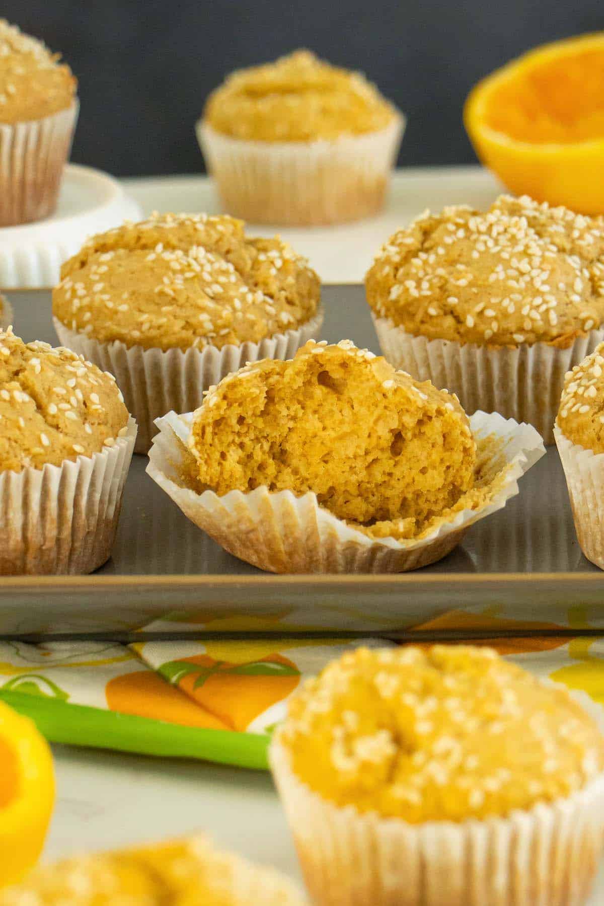 orange sesame muffins on a serving tray with oranges, one muffin torn in half, so you can see the texture inside