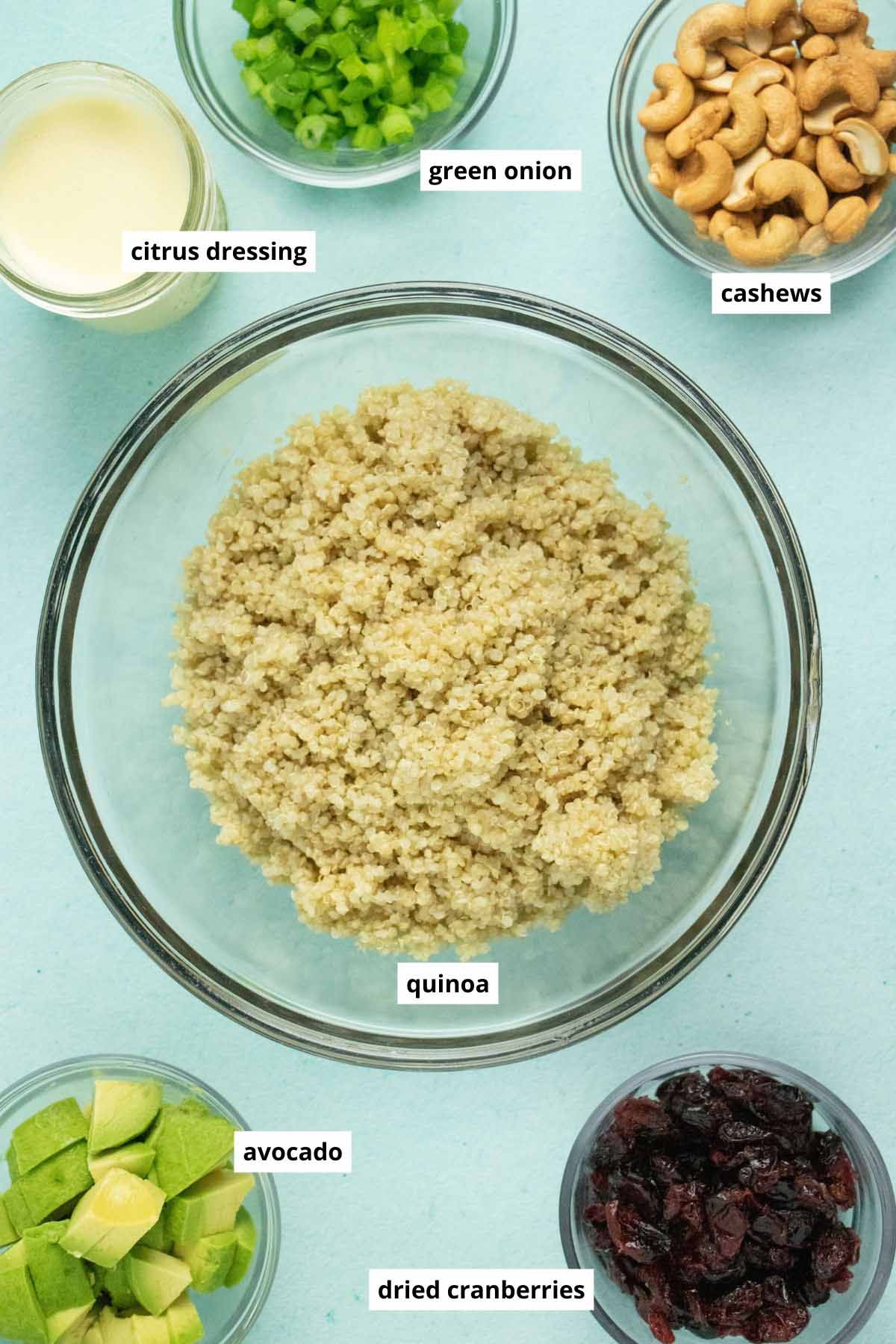 cooked quinoa, citrus dressing, and other salad ingredients in cups and bowls on blue table