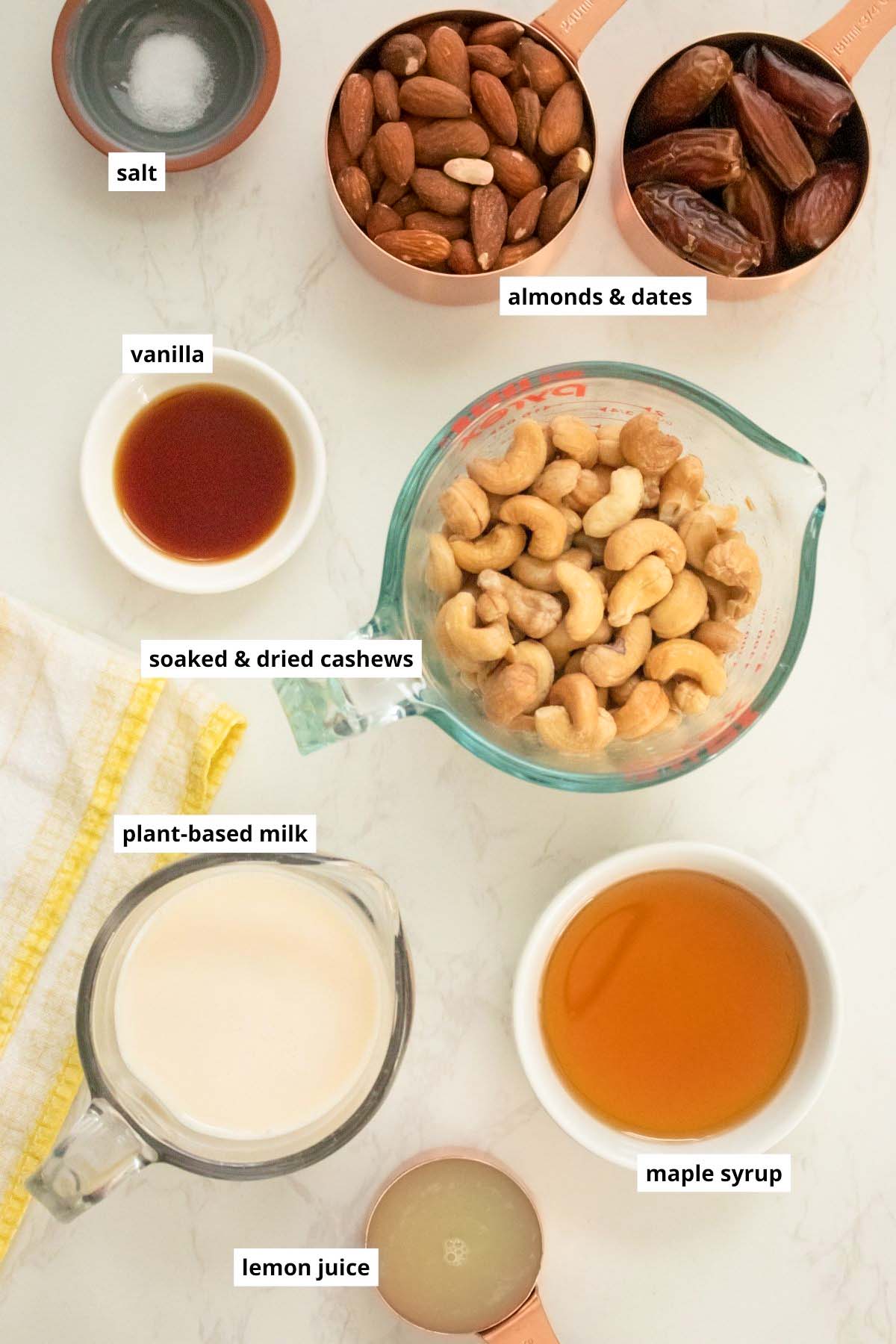 cashews, dates, almonds, and other vegan mini cheesecake ingredients in cups on a white table