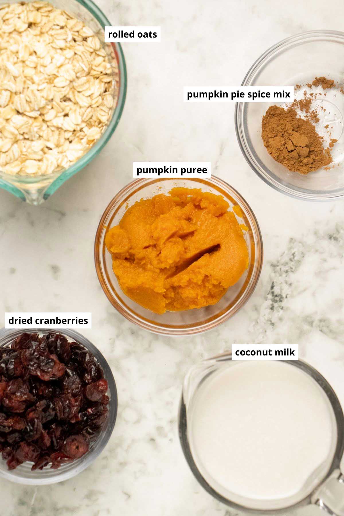 oats, pumpkin, pumpkin spice, dried cranberries, and coconut milk in cups on a white table with text labels