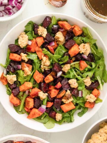 roasted beet and sweet potato salad with arugula and smashed chickpeas in a white bowl