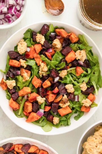 roasted beet and sweet potato salad with arugula and smashed chickpeas in a white bowl