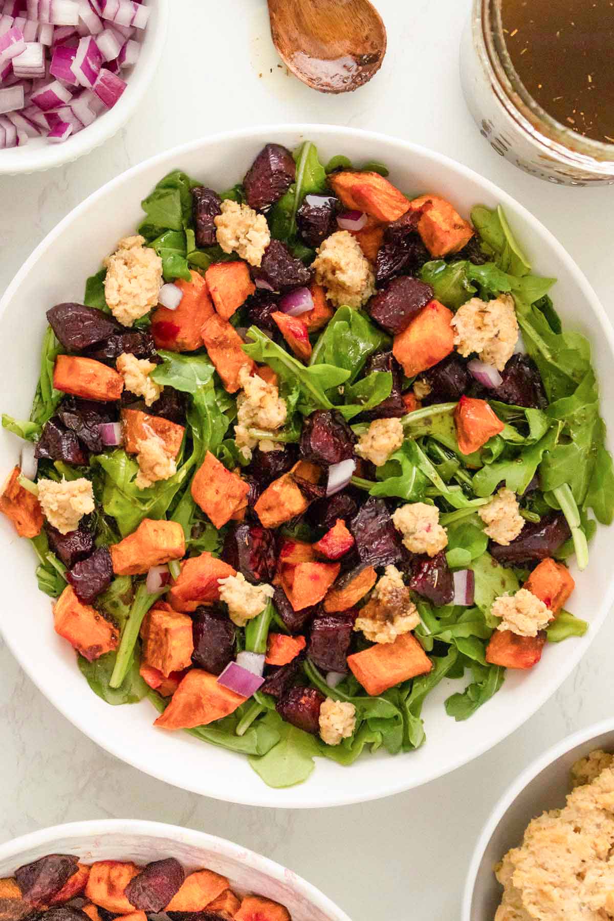 roasted beet and sweet potato salad with arugula and smashed chickpeas in a white bowl