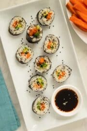 sweet potato sushi on a white plate with sesame seeds and soy sauce