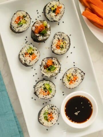 sweet potato sushi on a white plate with sesame seeds and soy sauce