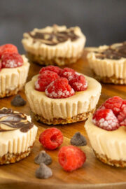 mini vegan cheesecakes on a wooden serving tray with raspberries and chocolate