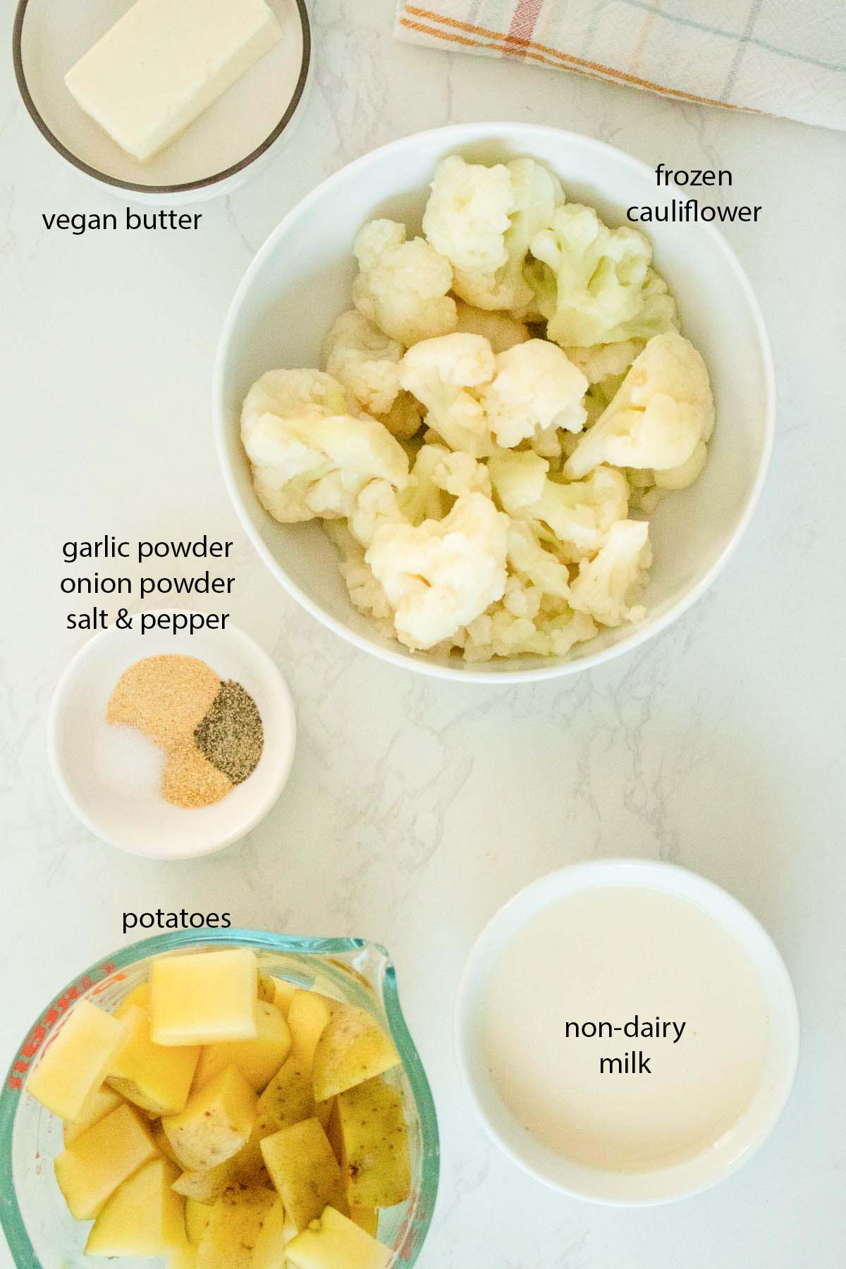 cauliflower, soy milk, spices, vegan butter, and potatoes in bowls on a white table