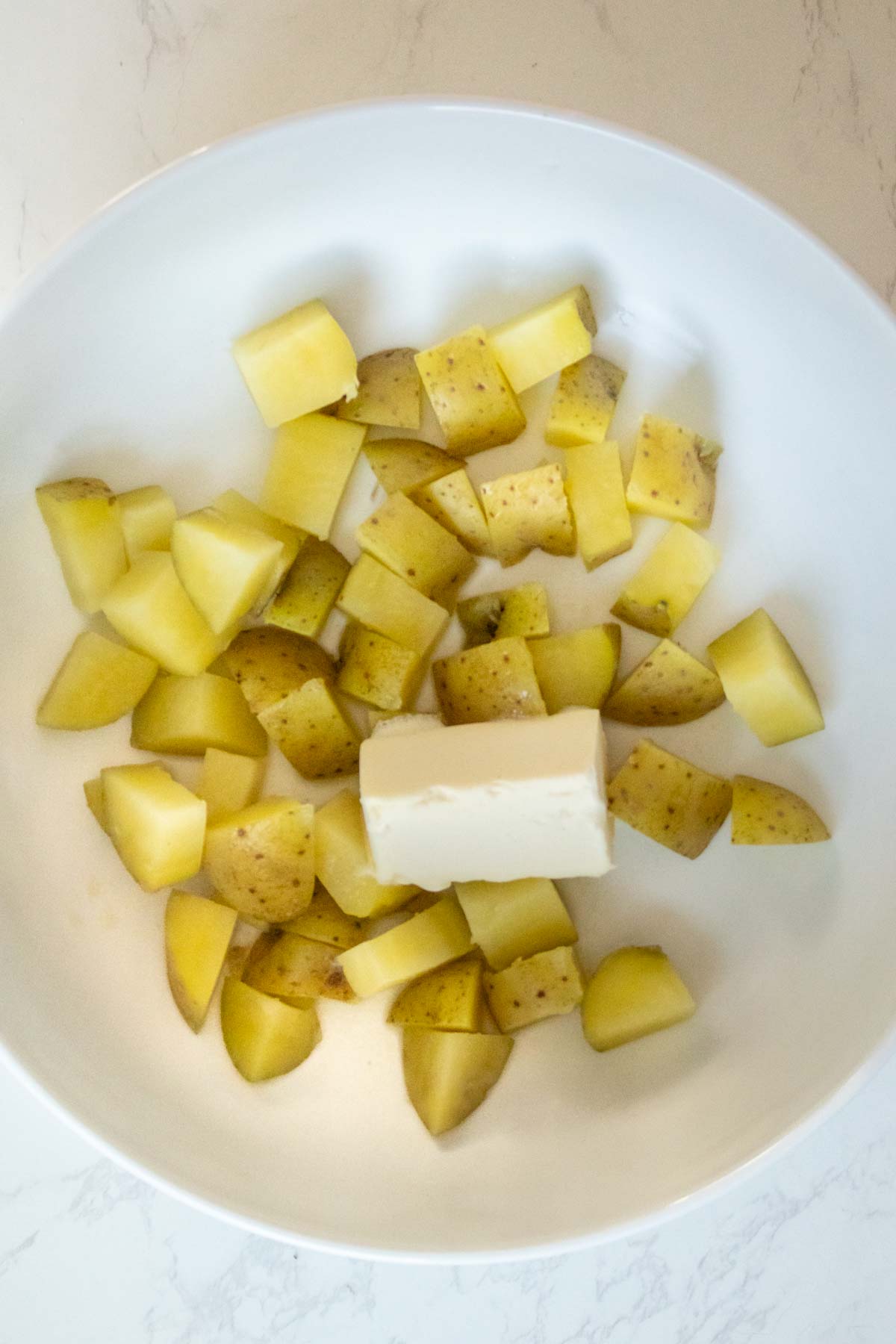 potatoes and vegan butter in the bowl before the first mash
