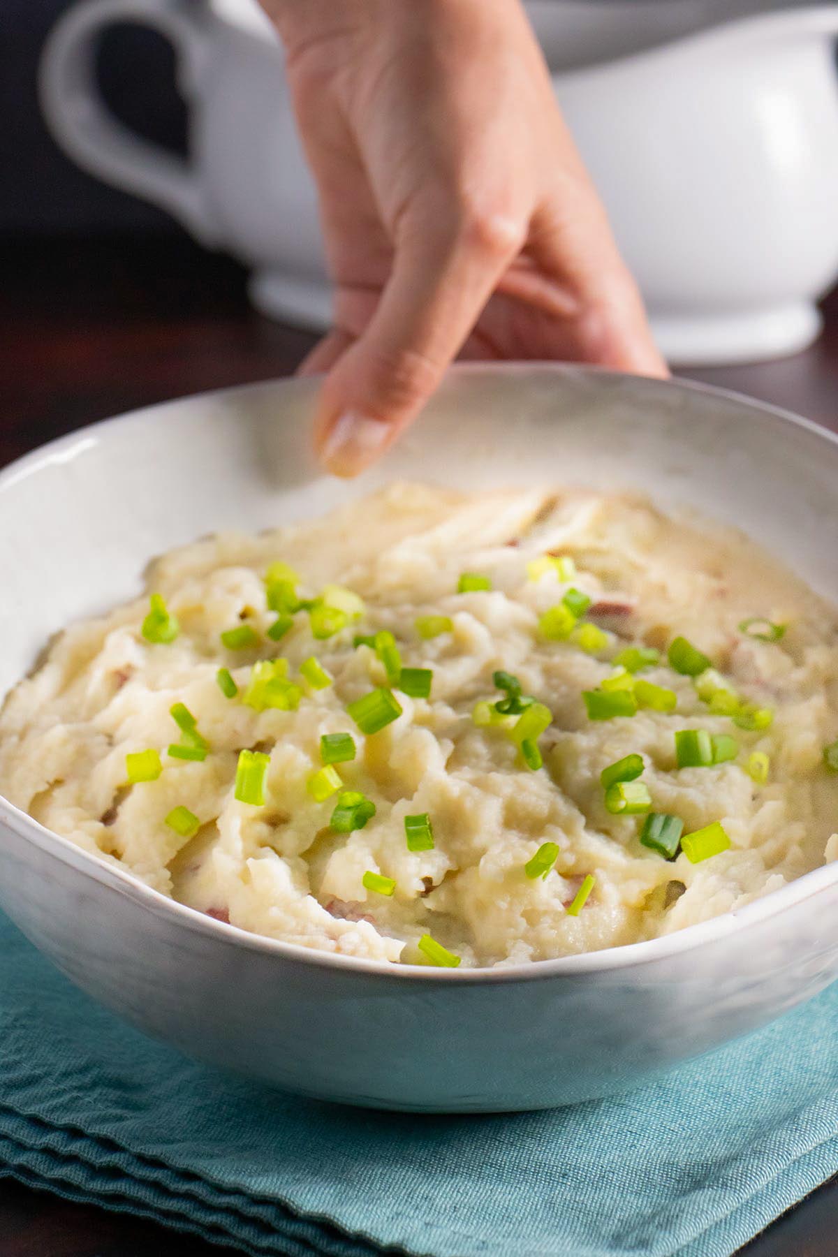 hand serving a bowl of cauliflower mashed potatoes