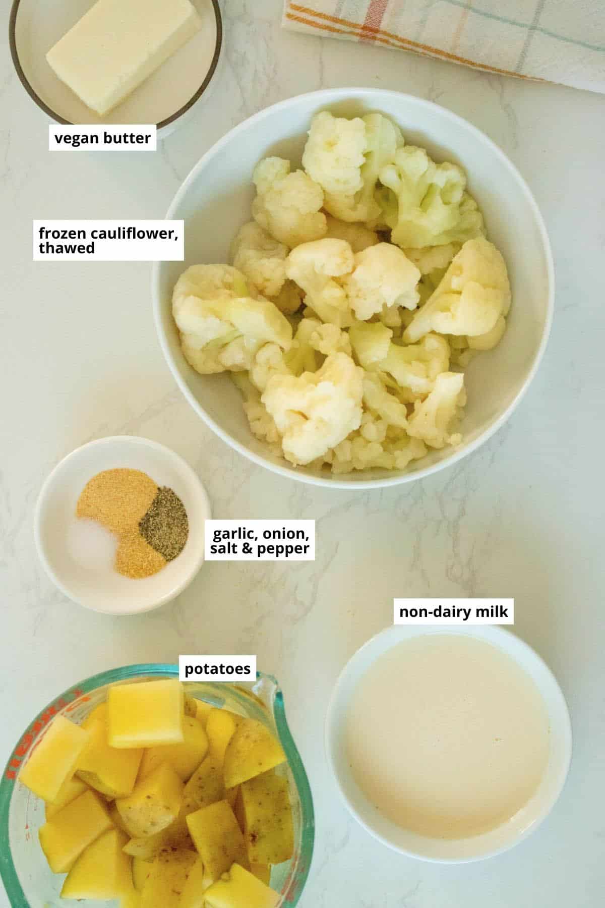 cauliflower, soy milk, spices, vegan butter, and potatoes in bowls on a white table