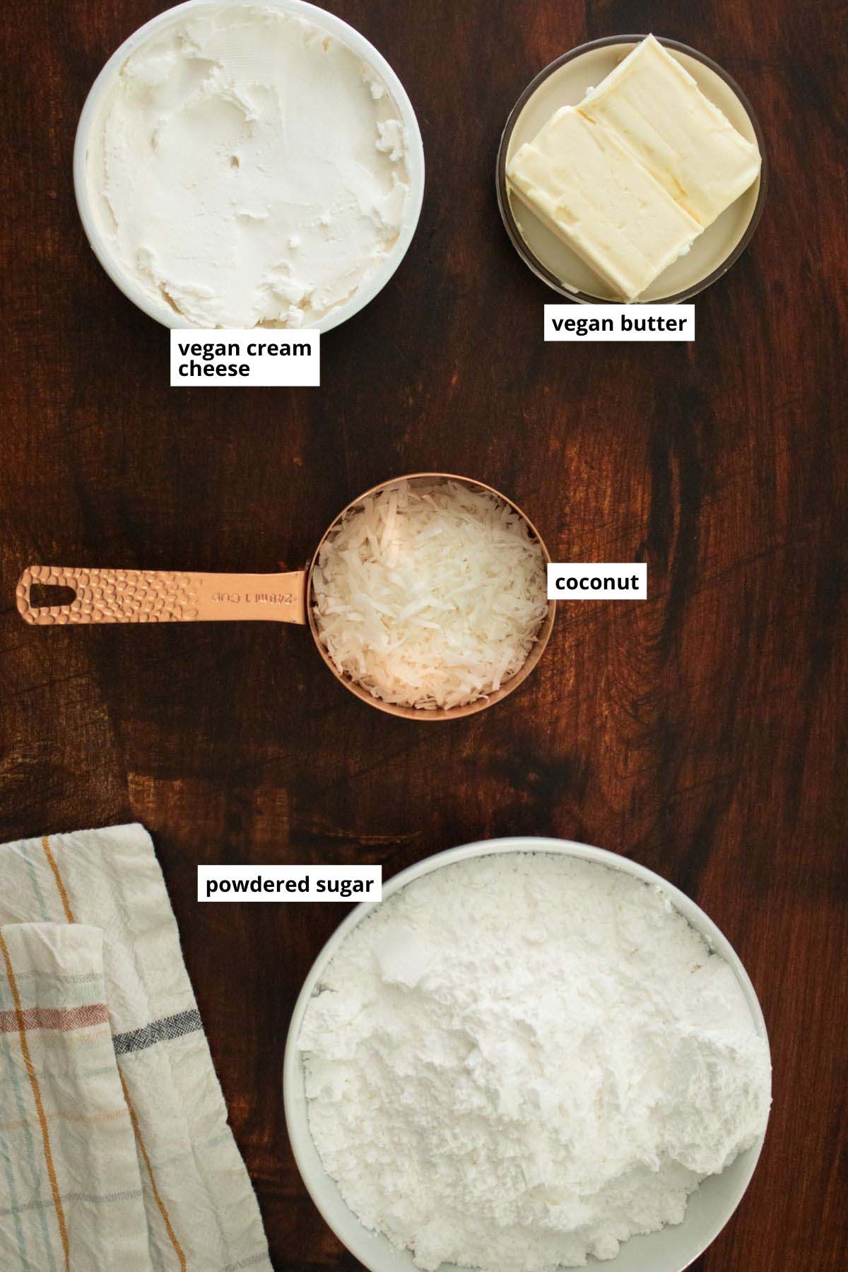 vegan cream cheese, coconut, and other frosting ingredients in cups on a wooden table