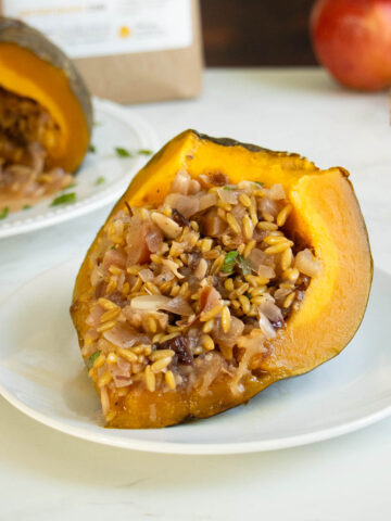 slice of stuffed kabocha squash on a plate with the whole squash in the background