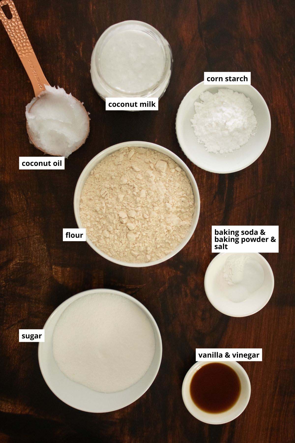 flour, coconut oil, coconut milk, and other coconut cupcake ingredients in cups on a wooden table