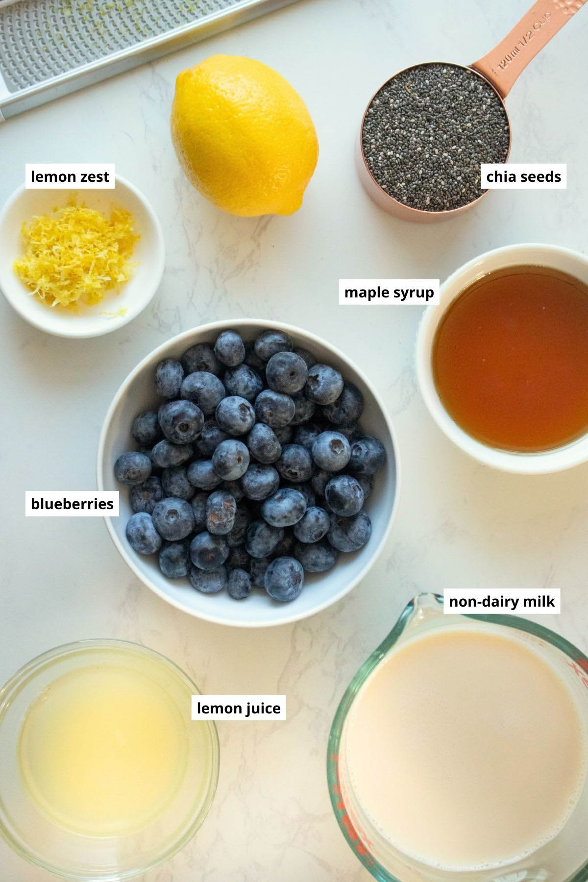 blueberries, lemon juice, lemon zest, chia seeds, non-dairy milk, and maple syrup in bowls on a white table