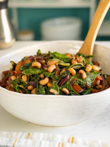 vegan black eyed peas and collards in a serving bowl with a wooden spoon