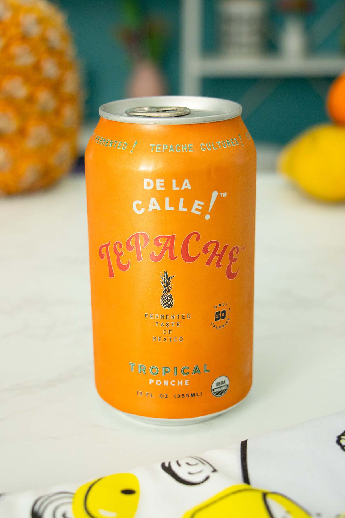 can of De La Calle Tepache Tropical Ponche on a white table with fruit in the background
