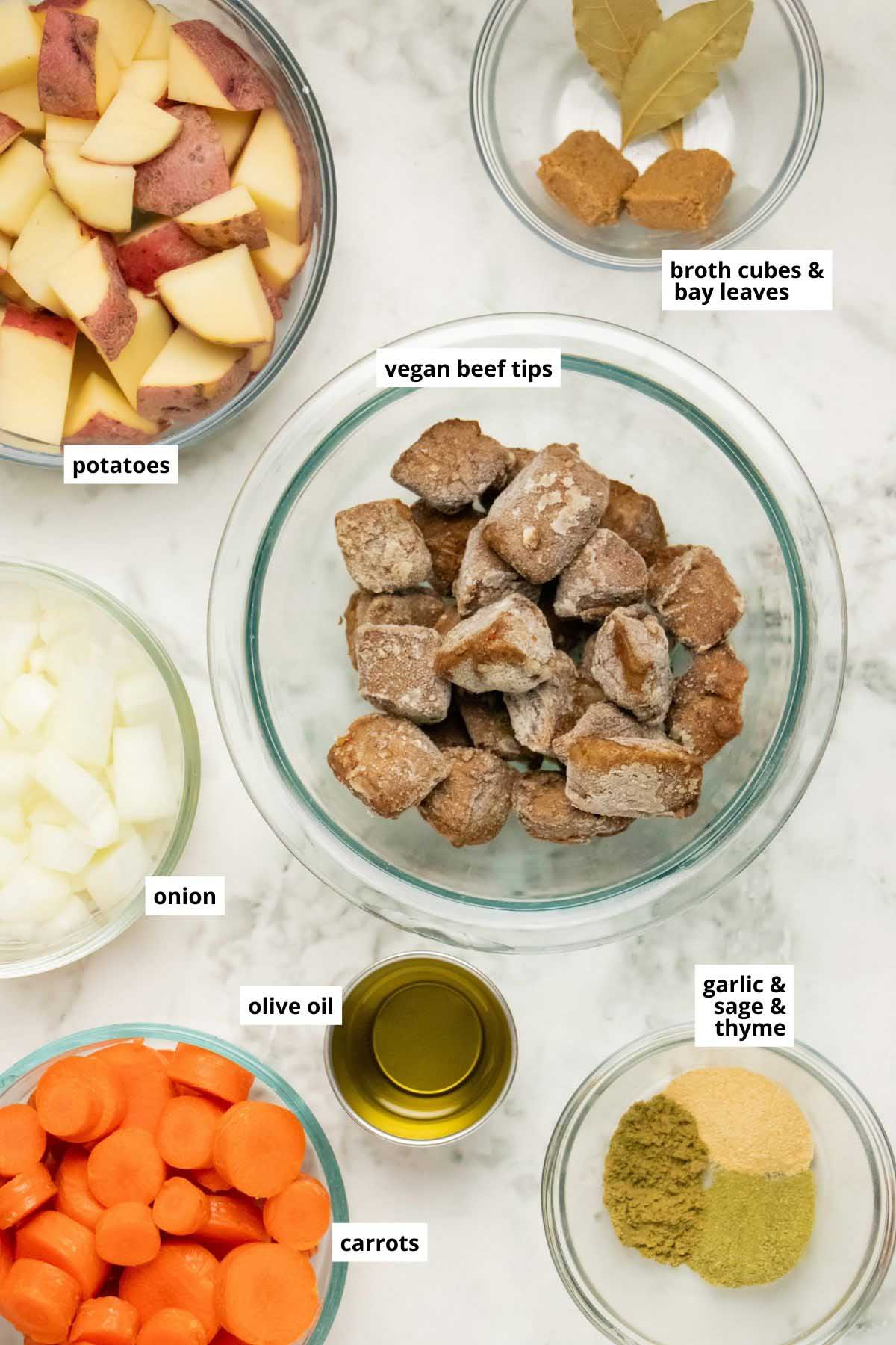 vegan beef tips, potatoes, carrots, and other stew ingredients in bowls on a white table