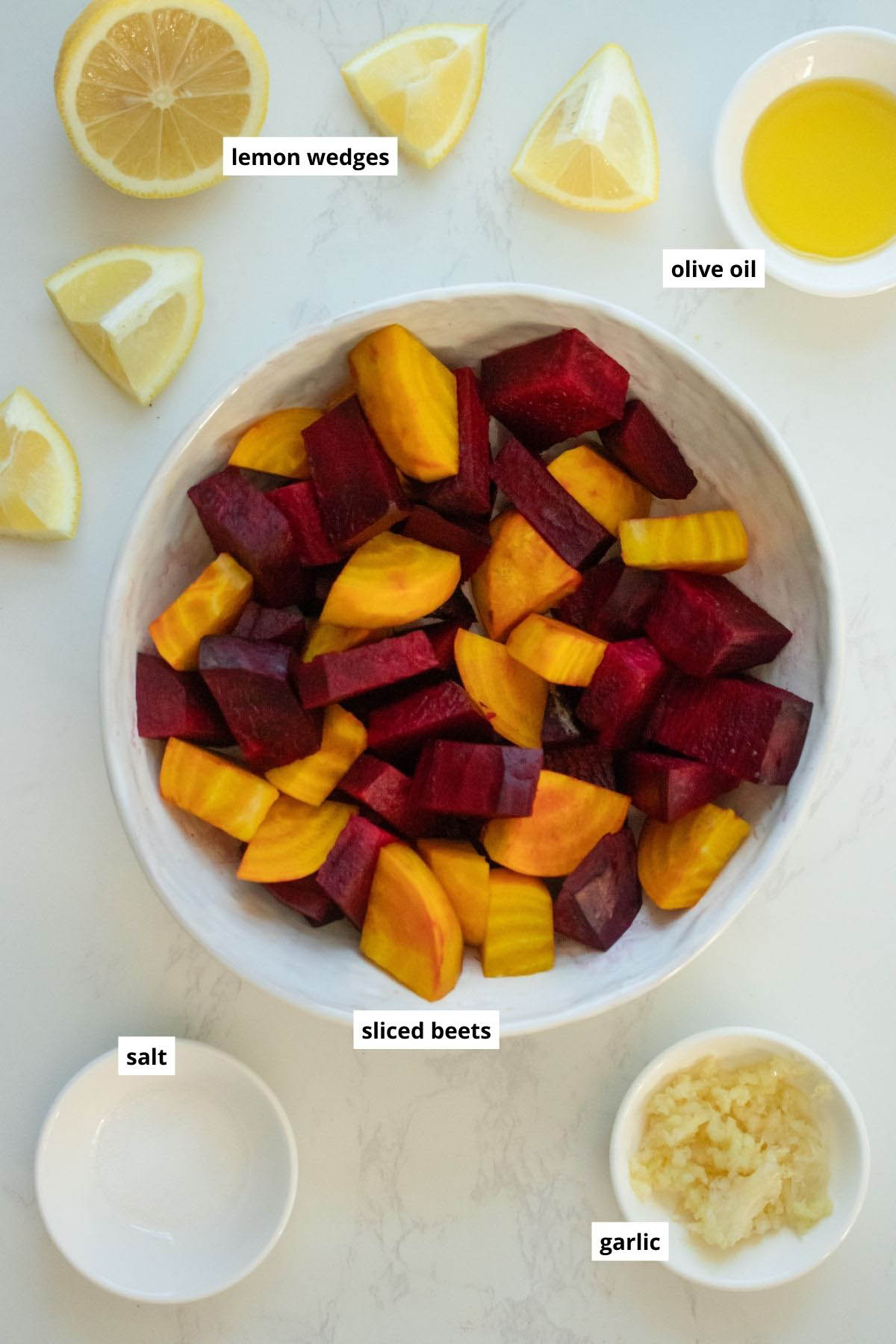 beets, garlic, oil, salt, and lemon wedges in bowls on a white table