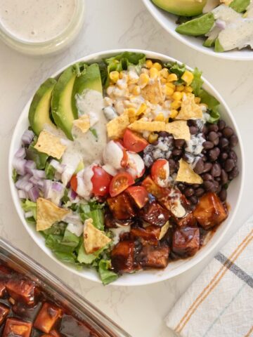 bbq tofu salad with avocado, beans, corn, tomato, and ranch dressing in bowls on a white table