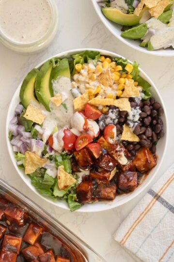 bbq tofu salad with avocado, beans, corn, tomato, and ranch dressing in bowls on a white table