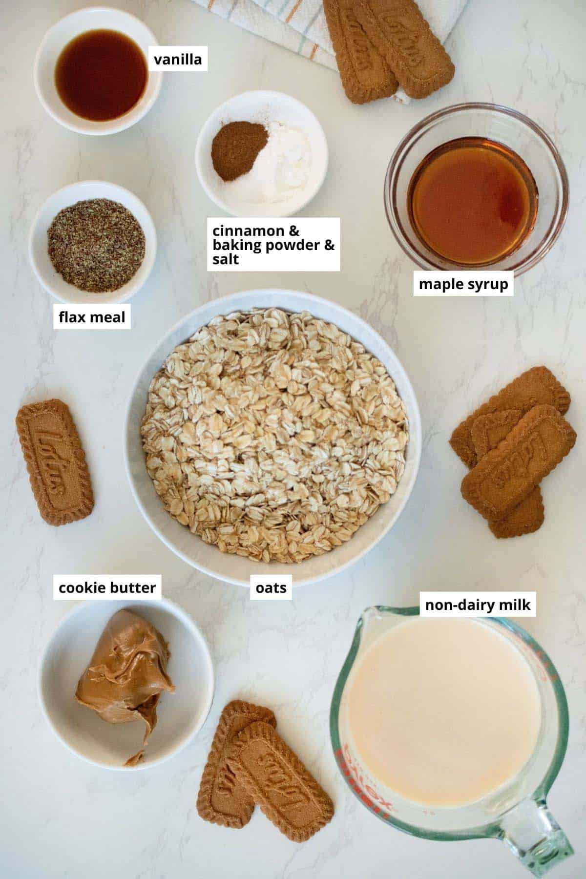 oats, cookie butter, and other baked oats ingredients in bowls on a white table