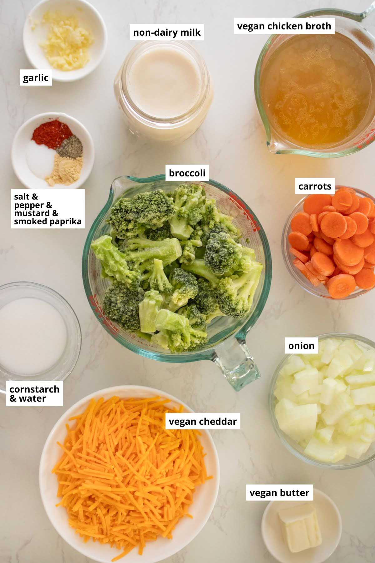 broccoli, vegan cheddar, and other soup ingredients in bowls on a white table